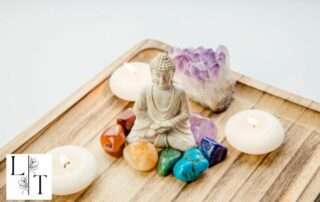 Statue de Bouddha entourée de pierres naturelles alignées selon les 7 chakras, symbolisant l’équilibre énergétique et l’harmonisation spirituelle